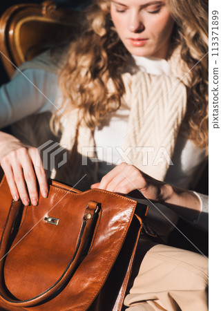 beautiful curly blond hair woman posing with a small shopper brown bag in a vintage chair 113371899
