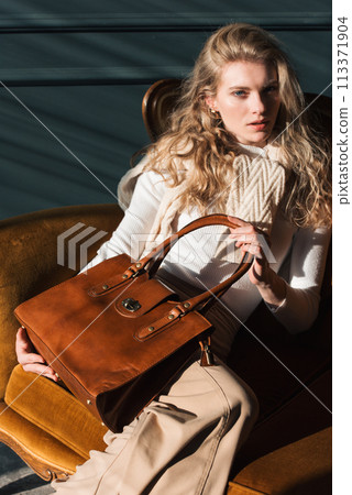 beautiful curly blond hair woman posing with a small shopper brown bag in a vintage chair beautiful curly blond hair woman posing with a small shopper brown bag in a vintage chair 113371904