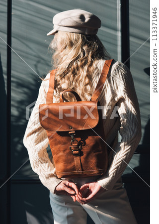 Studio portrait of beautiful woman with a curly blond hair holding brown backpack, posing on gray background. Studio portrait of beautiful woman with a curly blond hair holding brown backpack, posing on gray background. 113371946
