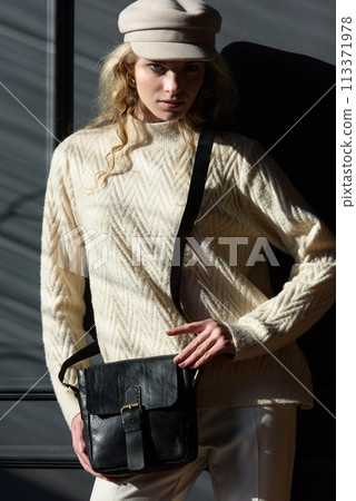 Studio portrait of beautiful woman with a curly blond hair holding black bag, posing on gray background. 113371978