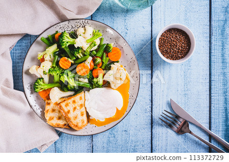 Mix of boiled vegetables, poached egg and waffle toast on a plate on the table top view Mix of boiled vegetables, poached egg and waffle toast on a plate on the table top view 113372729