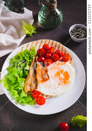 Grilled tacos with egg, fried bacon, vegetables and herbs on a plate on the table vertical view Grilled tacos with egg, fried bacon, vegetables and herbs on a plate on the table vertical view 113372737