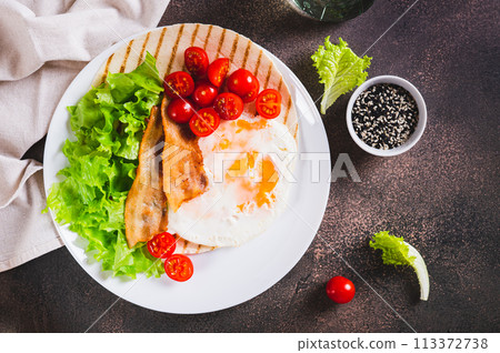 Appetizing tacos with fried egg, bacon, tomato and lettuce on a plate on the table top view 113372738
