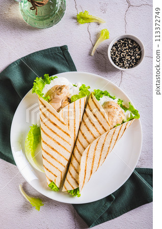 Grilled chicken fillet wrapped in tortilla with lettuce and sauce on a plate top and vertical view 113372749