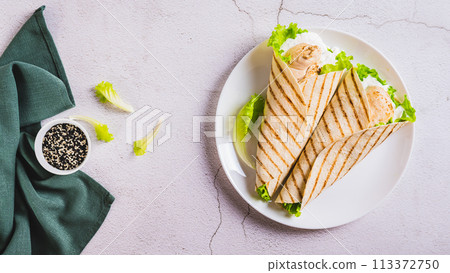 Grilled chicken fillet wrapped in tortilla with lettuce and sauce on a plate top view web banner Grilled chicken fillet wrapped in tortilla with lettuce and sauce on a plate top view web banner 113372750