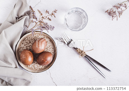 Naturally colored eggs for Easter on a plate, cutlery and a glass of water on the table top view Naturally colored eggs for Easter on a plate, cutlery and a glass of water on the table top view 113372754