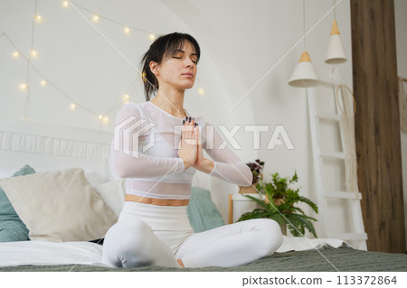 Yoga mindfulness meditation. Young healthy woman practicing yoga in bedroom at home. Woman sitting in lotus pose on bed meditating smiling relaxing indoor. Girl doing breathing practice. Yoga at home 113372864