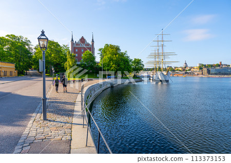 People walking along the waterfront near the historic Af Chapman ship moored in Stockholm on a clear day. Sweden 113373153
