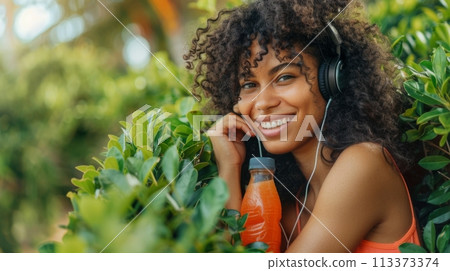 Happy woman enjoying music in a beautiful garden with a refreshing drink 113373374
