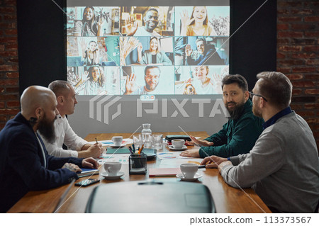 Team leaders gathering in conference room, having online video call to engage with remote employees. Effective remote communication strategies. 113373567