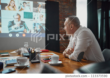 Businessman sitting in conference room and having online video call on TV screen with employees. Project discussion, planning 113373590