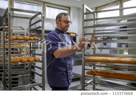 Man baker with trays of fresh bread in bakery. 113373668