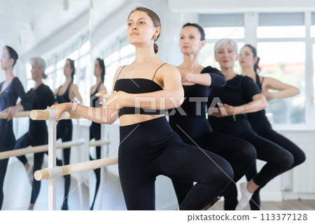 Young girl practicing in passe position at barre during group ballet class 113377128