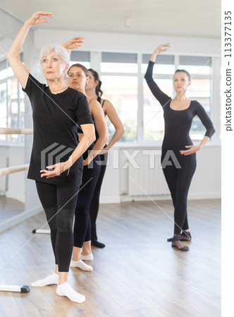 Teacher conducts class with girls in ballet studio, observes doing forth position exercise. Teacher conducts class with girls in ballet studio, observes doing forth position exercise. 113377135