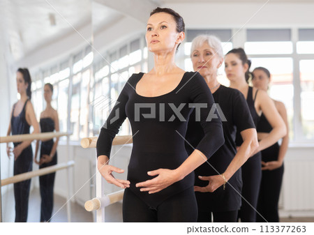 Girls in ballet class perform first position with participation of mature female mentor 113377263