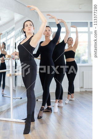 Graceful women of different ages practice at ballet stand in fifth position Graceful women of different ages practice at ballet stand in fifth position 113377280