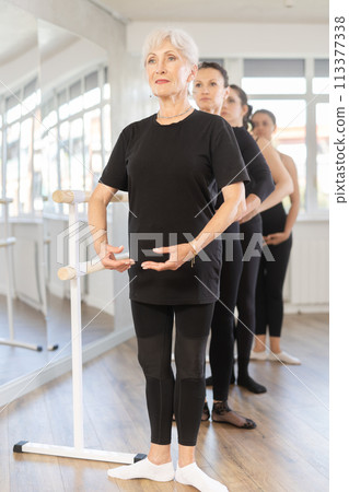 Elderly woman practicing basic ballet positions at group training Elderly woman practicing basic ballet positions at group training 113377338