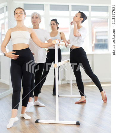 Teacher conducts class with girls in ballet studio, observes doing Batman exercise. 113377622