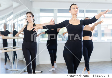 Young woman in group lesson with students rehearses, practices ballet dance, staging. Young woman in group lesson with students rehearses, practices ballet dance, staging. 113377701