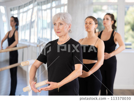 Women stand in fifth position near ballet barre during group training in dance studio 113378030