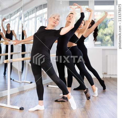 Elderly lady mastering battement tendu at barre during ballet class 113378075