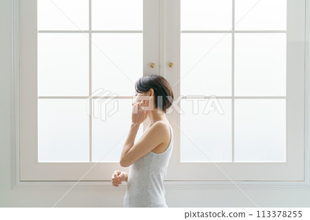 A woman in her 30s standing by the window A woman in her 30s standing by the window 113378255