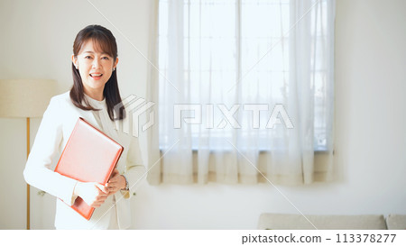 Middle-aged woman standing with a file in a casual room 113378277