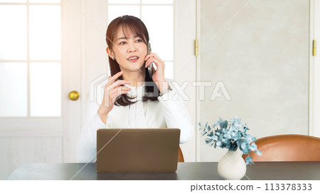 中年婦女在辦公室一邊看筆電一邊用智慧型手機說話 中年婦女在辦公室一邊看筆電一邊用智慧型手機說話 113378333