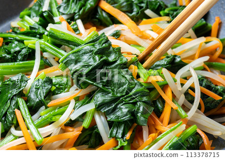 A cooking scene in which vegetables (spinach, carrots, and bean sprouts) are stir-fried in a frying pan. 113378715