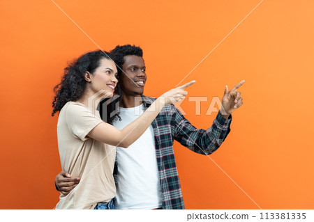 Happy Couple Pointing Together Against Orange Background Happy Couple Pointing Together Against Orange Background 113381335