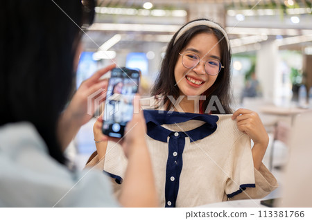 A woman taking a picture of her friend with a new clothe, having a fun shopping day together. 113381766