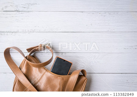Woman handbag with phone on white wood table. Woman handbag with phone on white wood table. 113382849