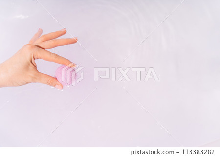 A woman's hand lowers a purple bath bomb into a bathtub of water A woman's hand lowers a purple bath bomb into a bathtub of water 113383282