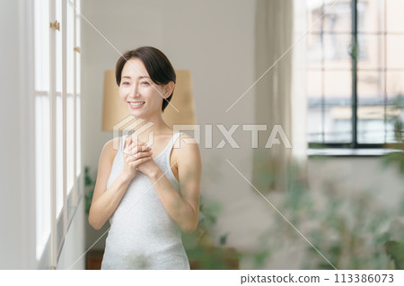 A woman in her thirties standing by the window 113386073