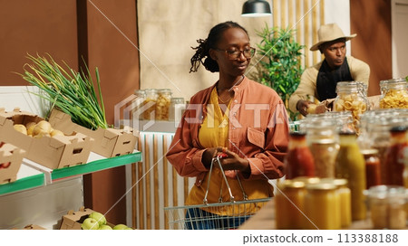 Regular customer searching for eco friendly food alternatives, looking at homemade ethically sourced bulk items at local supermarket. African american vegan woman going grocery shopping. Camera 1. 113388188