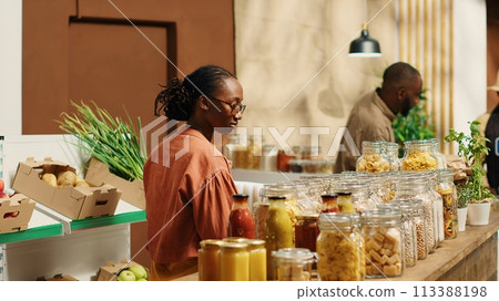 African american client examines bio homemade bulk products, looking to buy natural ethically sourced food alternatives for healthy nutrition. Woman shopping for goods at zero waste store. Camera 1. African american client examines bio homemade bulk products, looking to buy natural ethically sourced food alternatives for healthy nutrition. Woman shopping for goods at zero waste store. Camera 1. 113388198