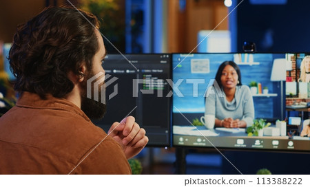Teleworking software engineer talking with colleagues during internet videocall, discussing ways to fix programming bugs. IT admin in videoconference meeting with coworkers, camera A Teleworking software engineer talking with colleagues during internet videocall, discussing ways to fix programming bugs. IT admin in videoconference meeting with coworkers, camera A 113388222