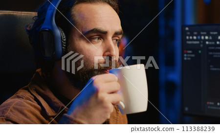 Developer listening music and drinking coffee while doing programming during remote job shift in home office. IT expert enjoying audio podcast and hot beverage, working on PC, camera A close up 113388239