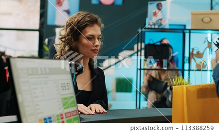 African american retail clerk scanning barcode on bag at cash register, preparing items for customer at department store. Young woman choosing trendy accessories from showroom. Camera A. 113388259