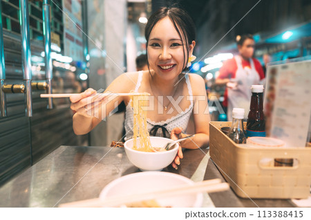 Asian foodie tourist woman eating wonton noodles at China town asia street food night market 113388415