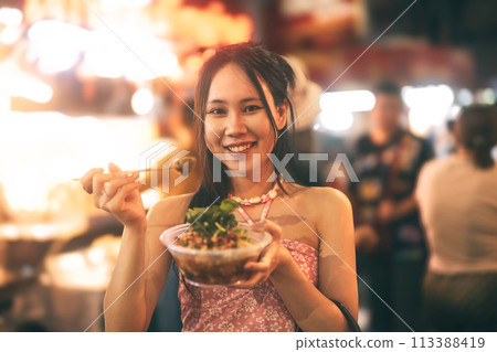 Asian foodie tourist woman eating spicy grilled squid at China town asia street food night market 113388419