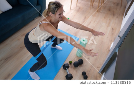 Young woman squatting with elastic band on her legs at home Young woman squatting with elastic band on her legs at home 113388516