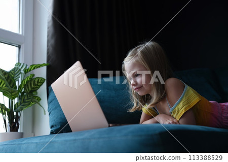 Little girl lying on couch and looking at laptop screen 113388529