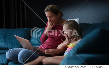 Surprised mom and daughter are sitting on couch and looking at laptop screen 113388530