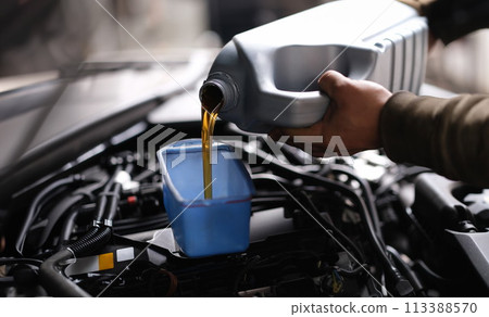 Master repairman pouring motor oil into car engine closeup 113388570