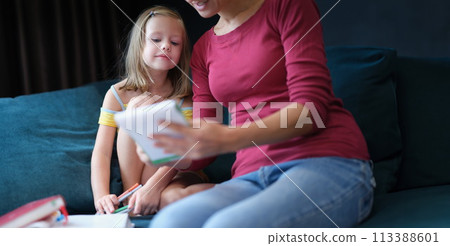 Little girl and woman sitting on couch with textbooks Little girl and woman sitting on couch with textbooks 113388601