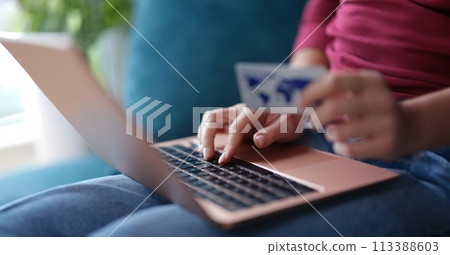 Woman typing on laptop keyboard and holding credit bank card in her hands closeup 113388603