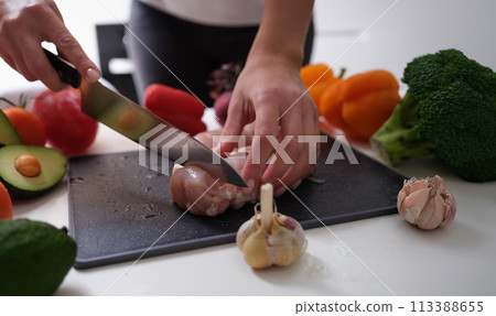 Chef cutting meat on board near vegetables closeup Chef cutting meat on board near vegetables closeup 113388655
