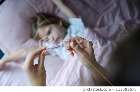 Woman hand holding mercury thermometer with high temperature against background of sick girl closeup Woman hand holding mercury thermometer with high temperature against background of sick girl closeup 113388675