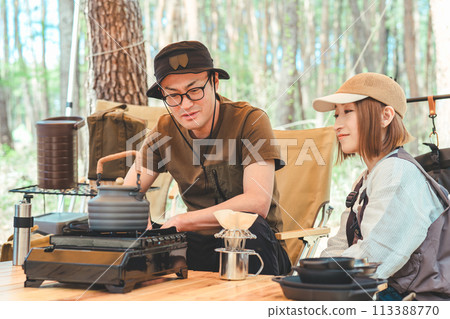 Camper couple, man and woman, making coffee using a coffee grinder at a campsite Camper couple, man and woman, making coffee using a coffee grinder at a campsite 113388770